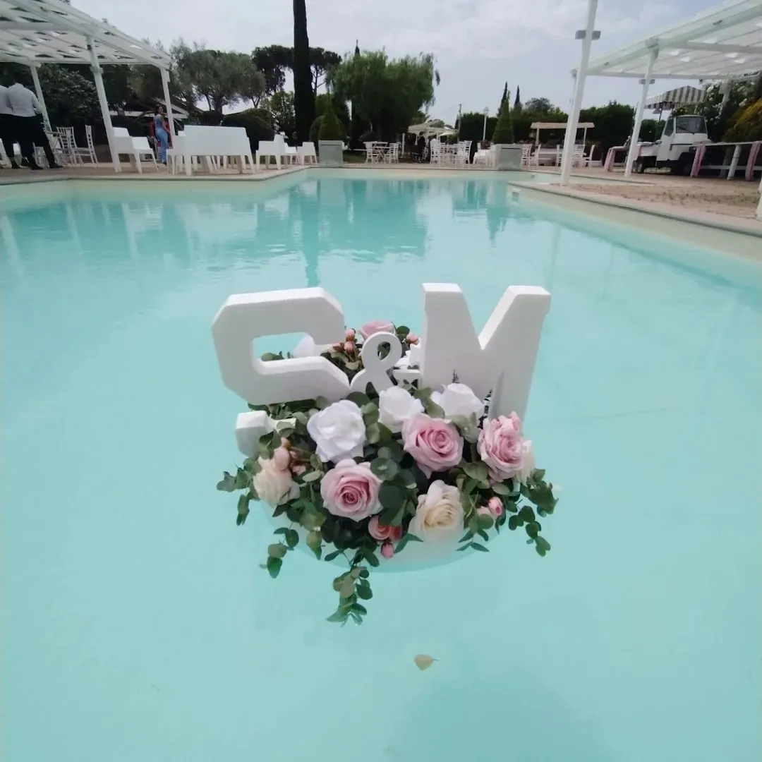 Composizione di rose rosa e bianche galleggiante in piscina con le iniziali degli sposi