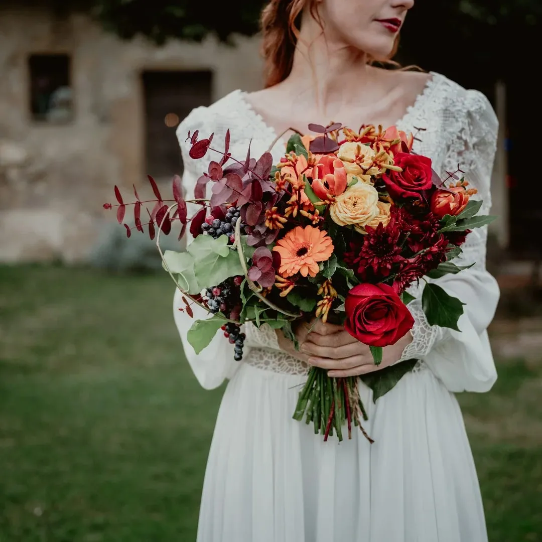 Bouquet da sposa autunnale con rose rosse, gerbere arancio e foglie bordeaux
